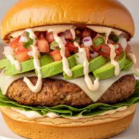 The Baja Turkey Burger from the First Watch Breakfast Menu with Prices, featuring a seasoned turkey patty, avocado, mixed greens, pico de gallo, and a spicy chipotle mayo on a brioche bun.