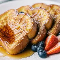 French Toast from the First Watch Breakfast Menu with Prices, made with thick-cut brioche, topped with powdered sugar and served with warm syrup.