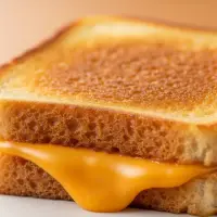 Grilled Cheese from the First Watch Breakfast Menu with Prices, made with melted cheddar on toasted artisan bread, served with a side of fruit.