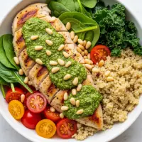 Pesto Chicken Quinoa Bowl from the First Watch Breakfast Menu with Prices, made with quinoa, grilled chicken, kale, shredded carrots, tomatoes, and basil pesto, topped with feta cheese.