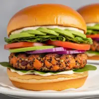 Veggie Burger from the First Watch Breakfast Menu with Prices, featuring a house-made patty with vegetables and grains, topped with avocado, mixed greens, tomato, and red onion on a brioche bun.